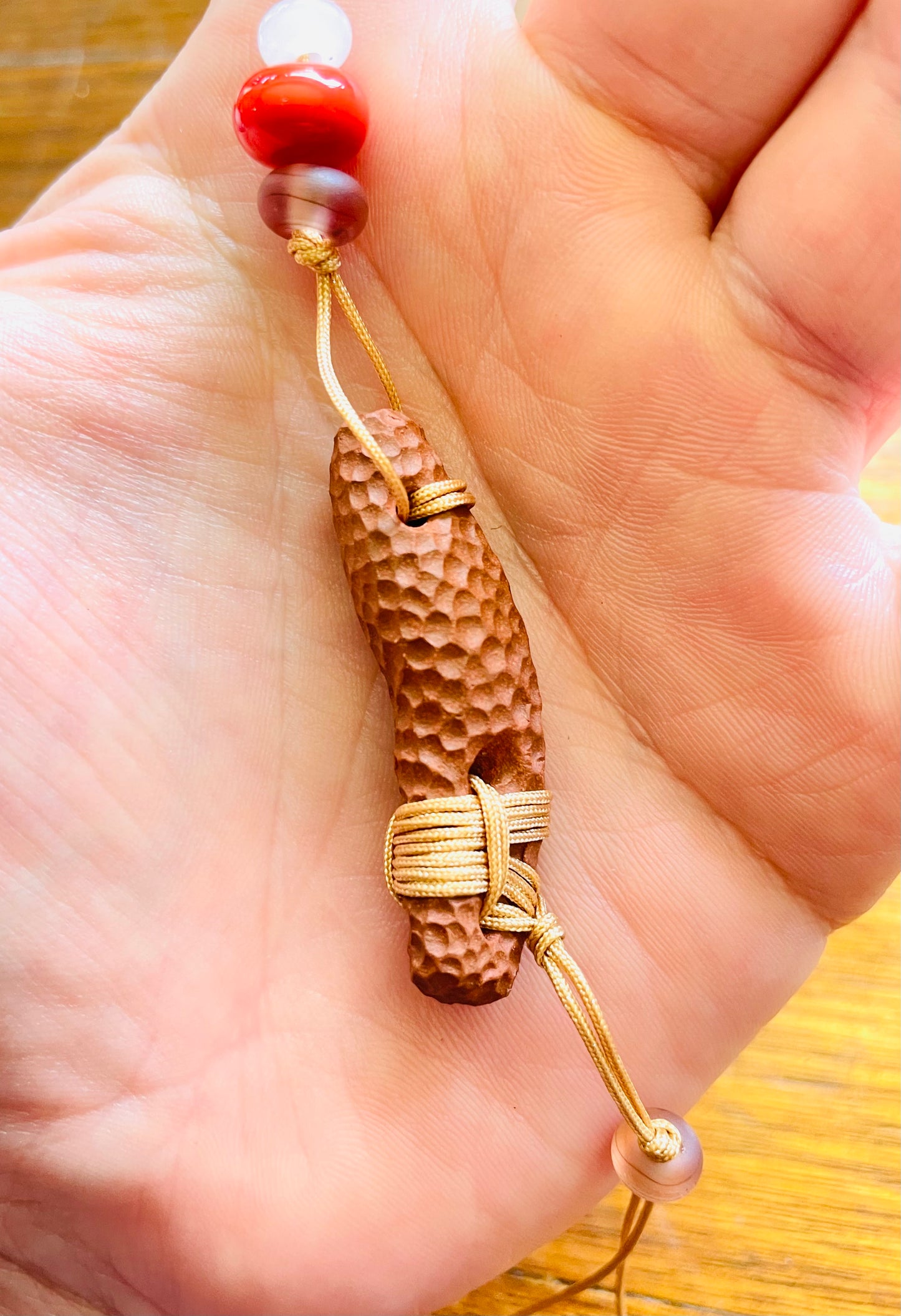 Close-up photo of a ceramic pendant necklace in the palm of a hand, highlighting the natural beauty of the pendant and the skilful way the cord is tied off with beads, showcasing the organic and handmade qualities.