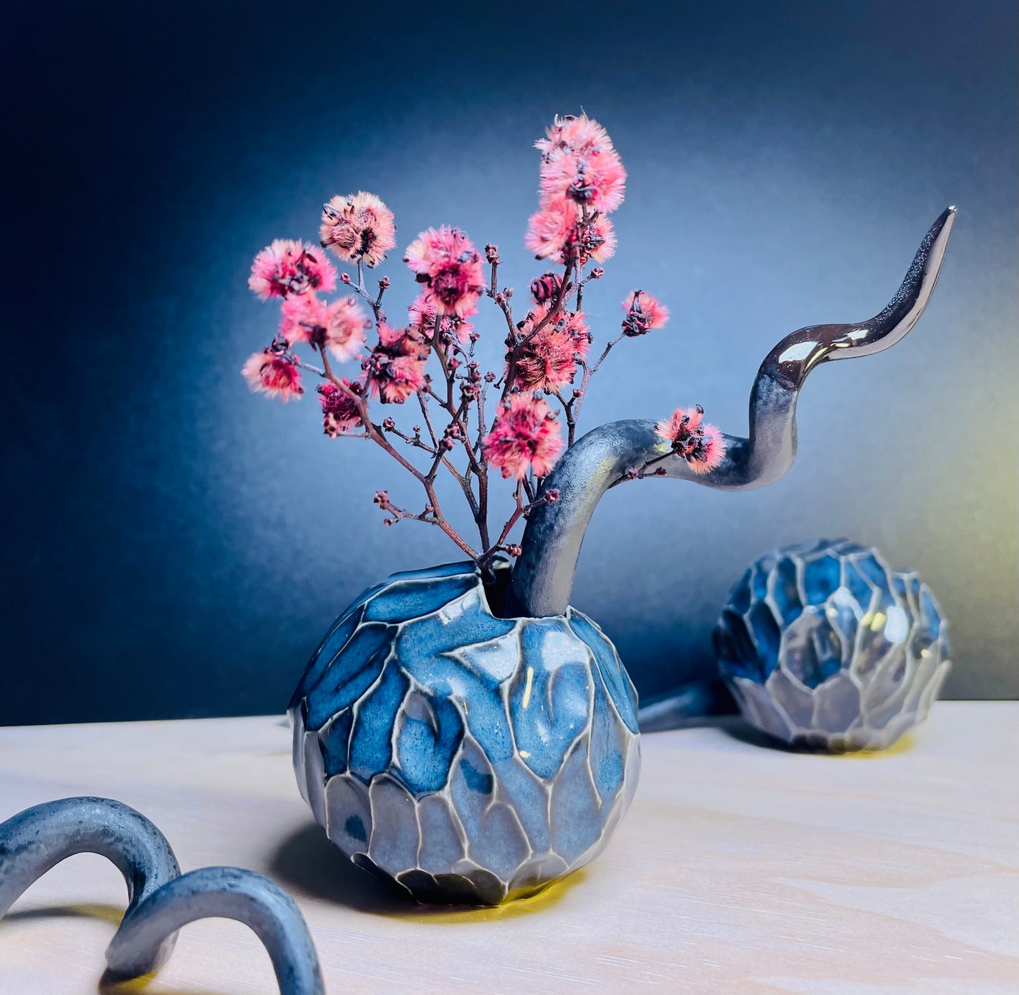 Blue porcelain ball vases, hand-carved with precision, placed in a decorative setting with one vase on its side, surrounded by pink dry flowers and other ornaments, emphasising the artisanal craftsmanship and natural beauty of the scene.