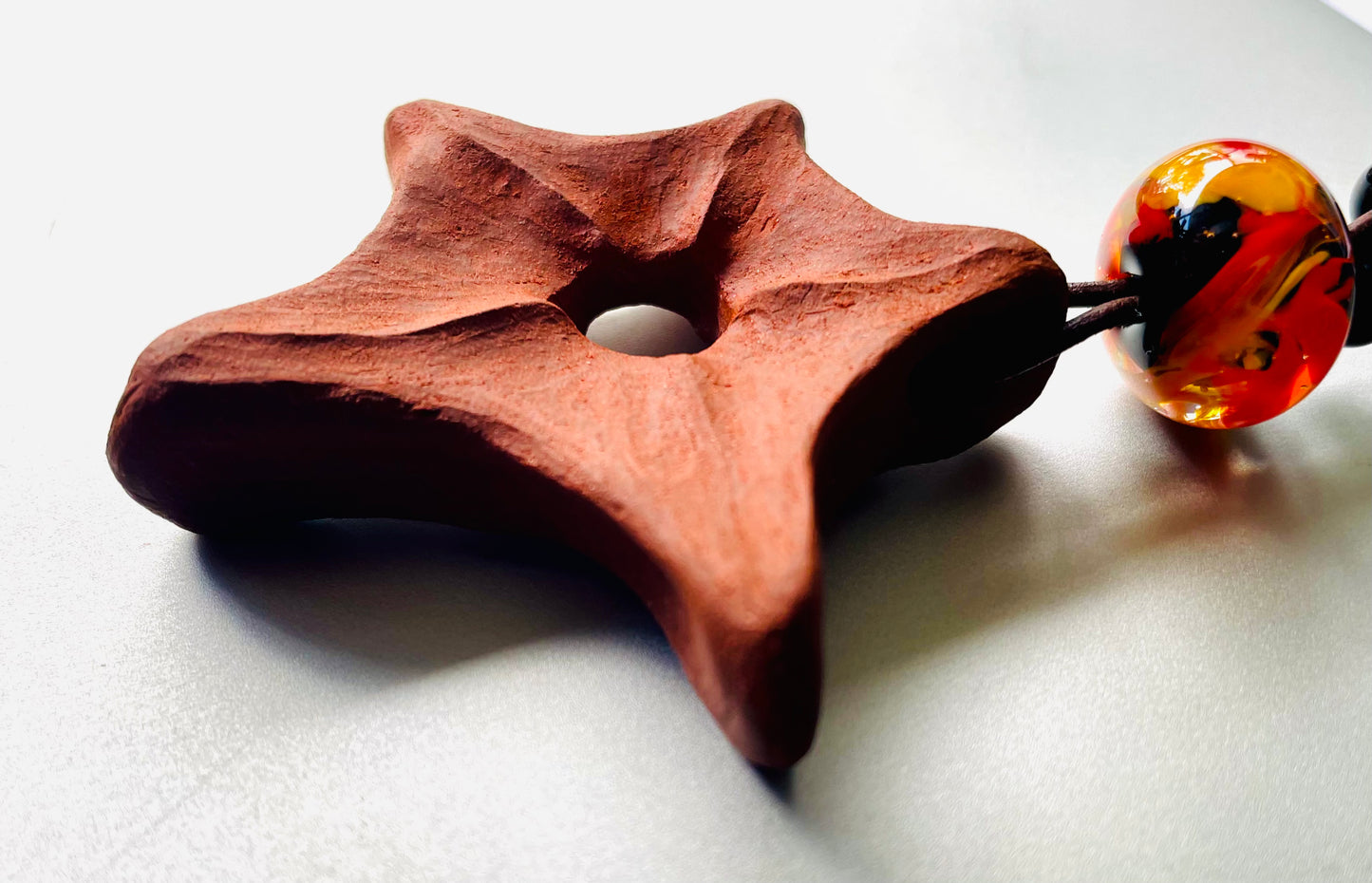 Ceramic star pendant, hand-carved and adorned with glass beads, viewed in close-up and from the side to emphasise the intricate details and artisanal charm of the piece.