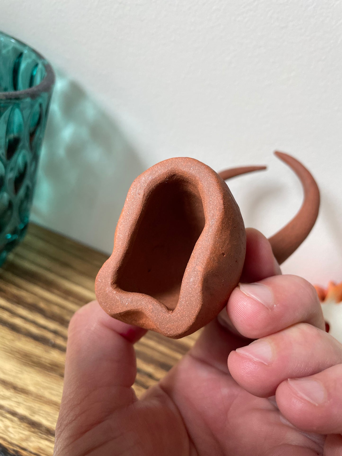 Yak figurine crafted from red earth clay, featuring a minimalistic design and a natural finish, held in a person's hand and viewed from the bottom to showcase its hollow interior, highlighting the artisanal craftsmanship and unique character of the piece.