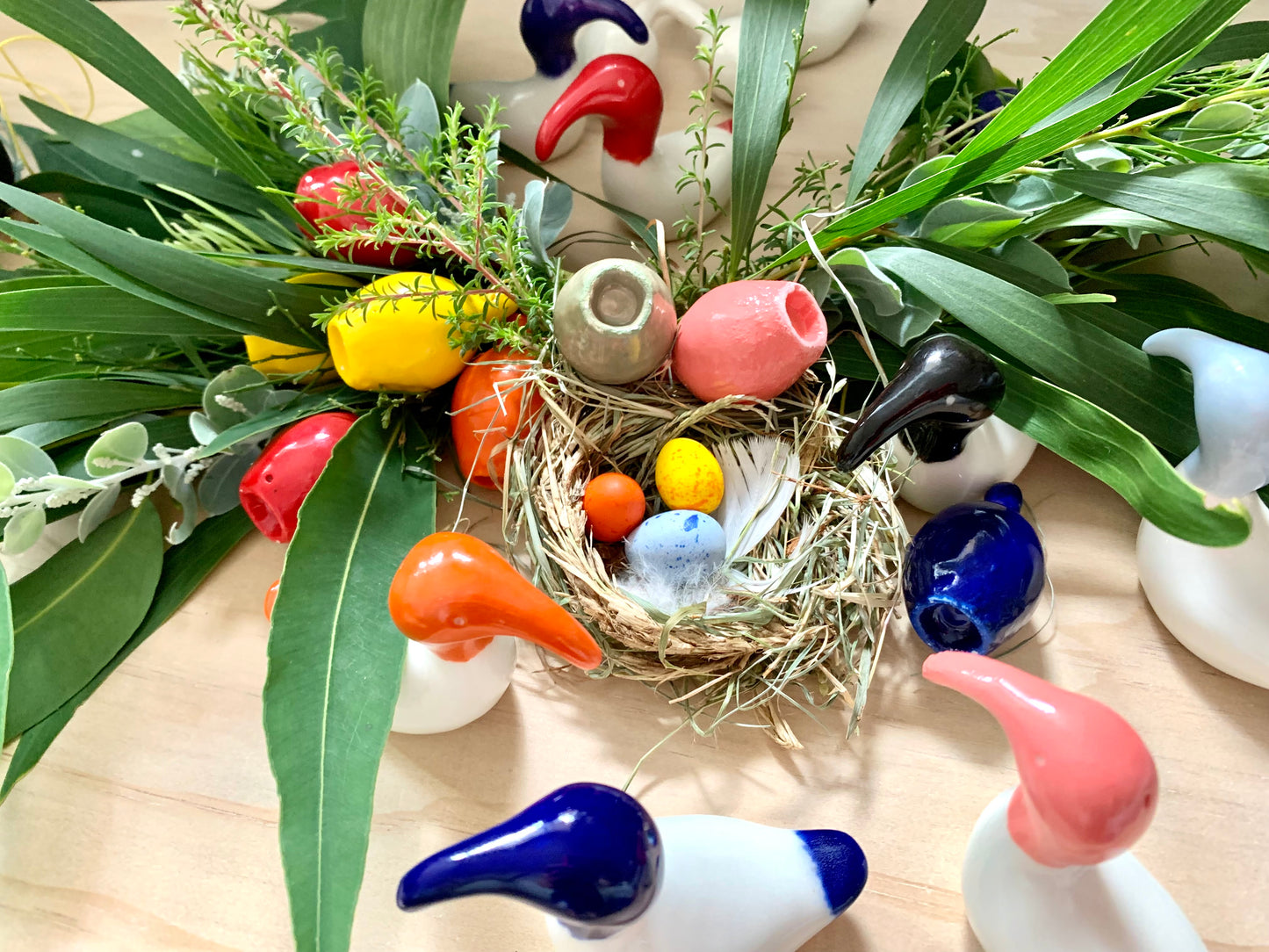 Ceramic artwork depicting a red Australian White Ibis near a nest, adorned with Easter eggs and set against a backdrop of green leaves and colourful accents in pink, blue, and orange.