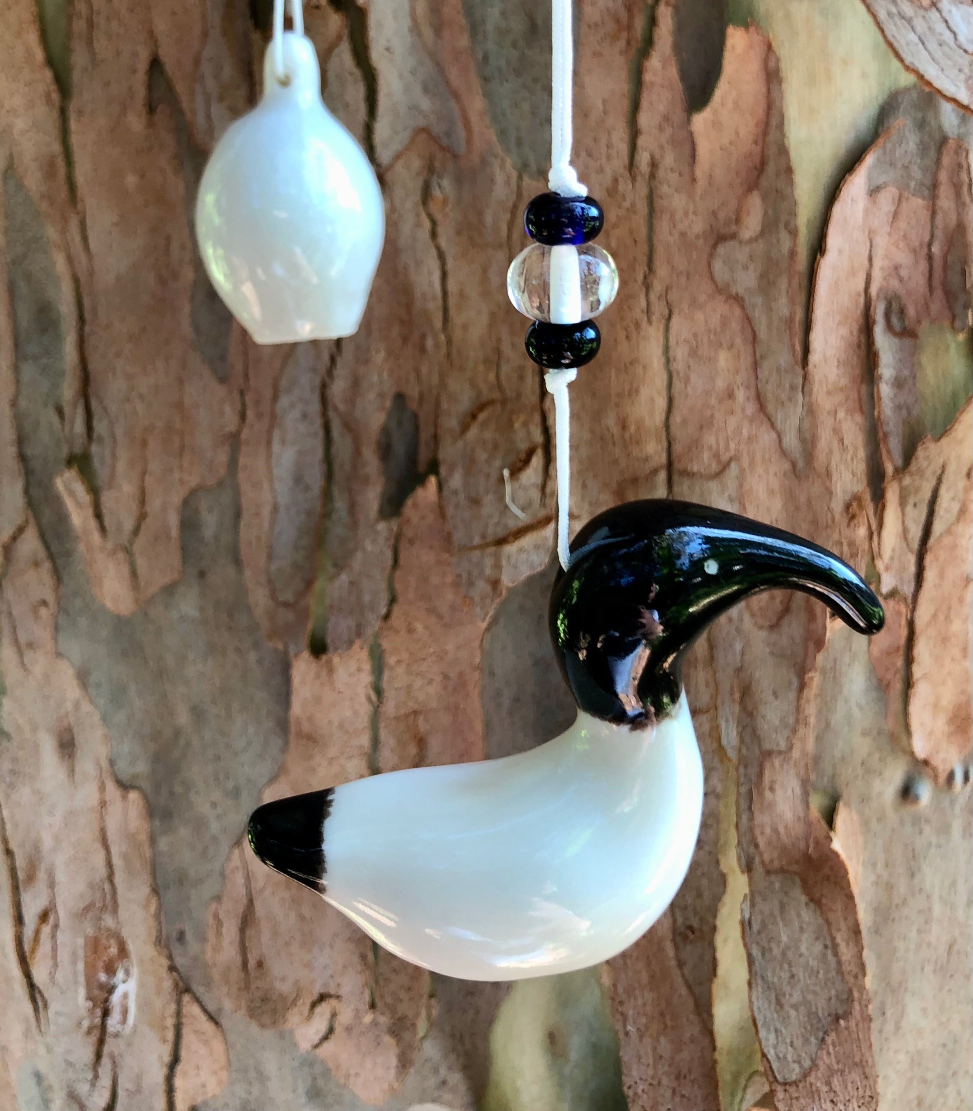 Artistic black ceramic representation of an Australian White Ibis hanging from a tree, complemented by a vibrant glass ceramic bead, blending nature and craftsmanship.