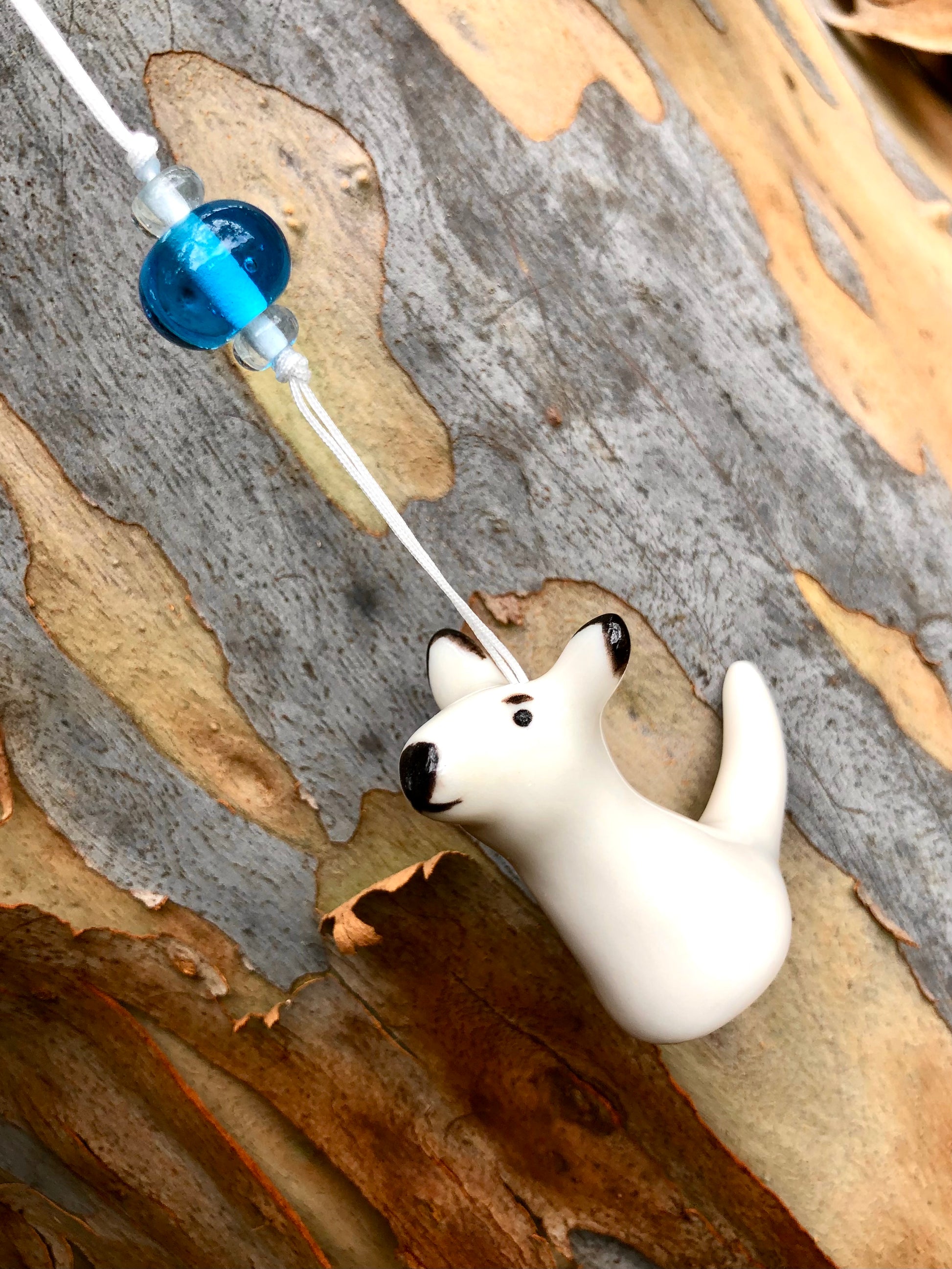 Ceramic kangaroo ornament suspended from a tree branch, nestled against the rough bark, adding a touch of Australian charm to the natural surroundings and creating a visually appealing outdoor scene.