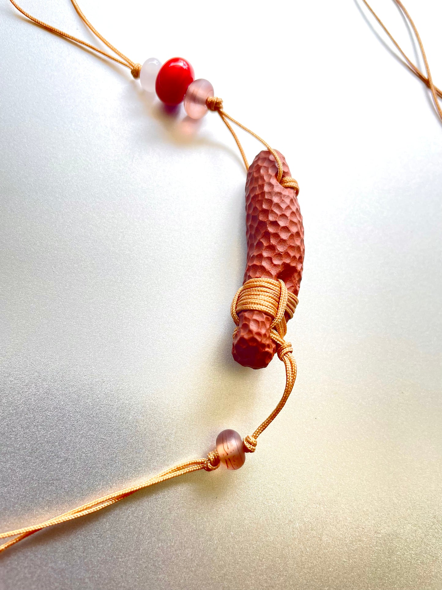 Close-up photo showcasing the natural beauty and craftsmanship of a ceramic necklace pendant, featuring a gold cord carefully tied off with beautiful beads, highlighting the intricate details and earthy charm of the piece.