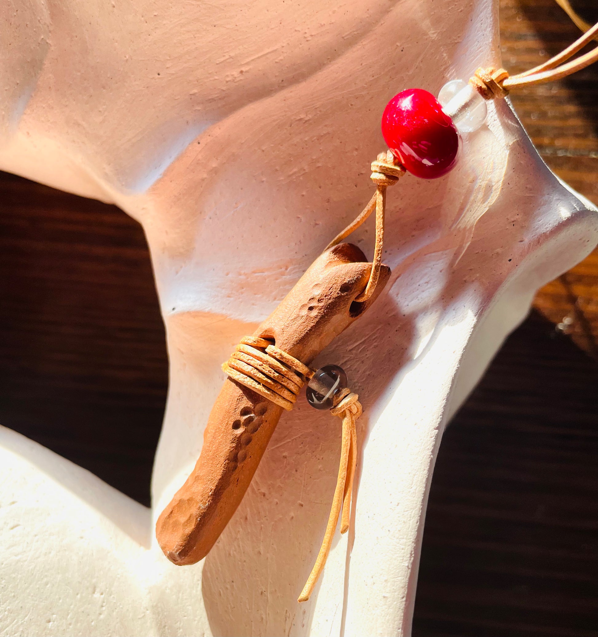 Rustic ceramic pendant handmade from red earth clay, adorned with a red bead that mimics wood and complemented by Italian glass beads, finished with a light brown leather cord for a natural and elegant appearance.