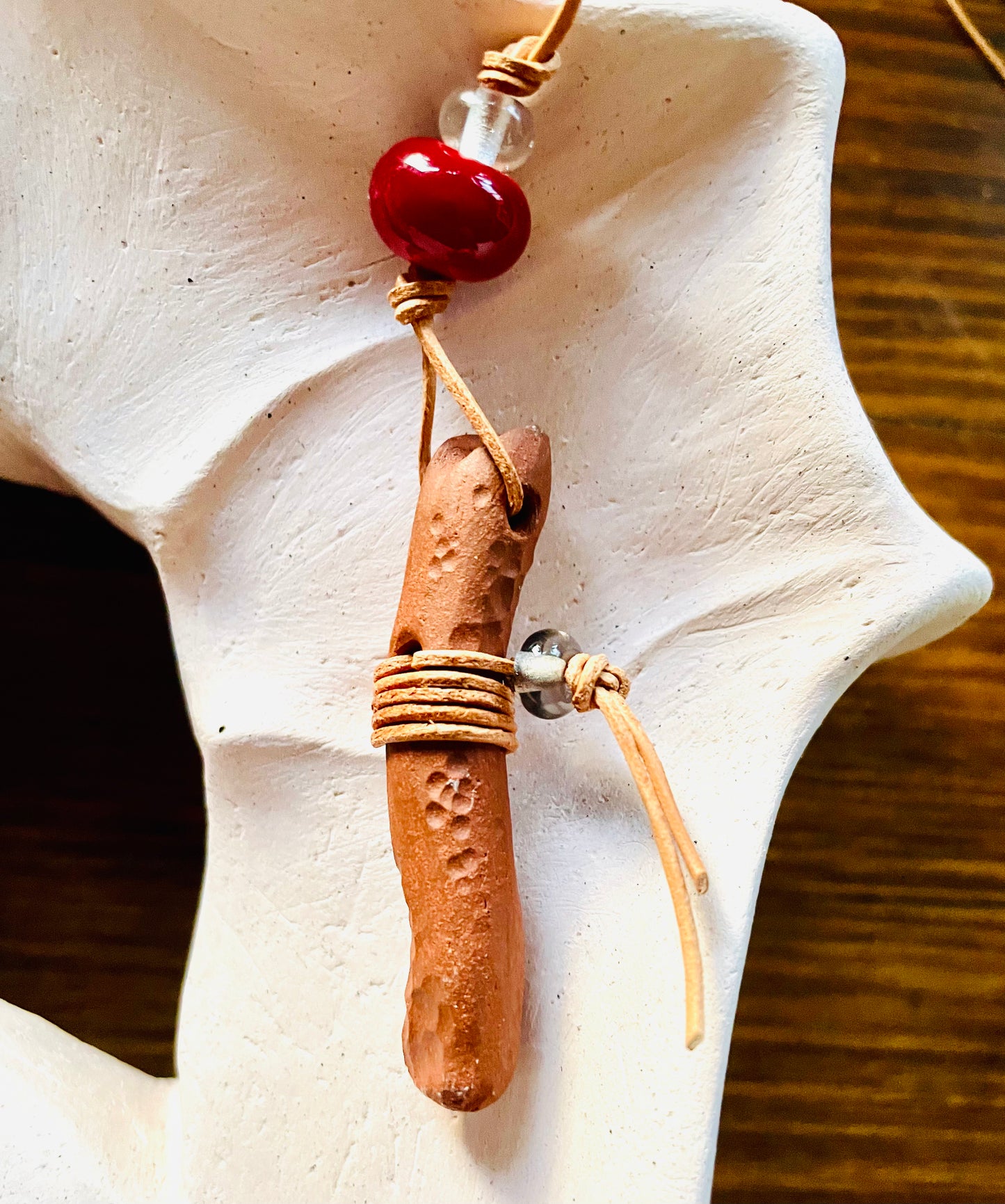 Ceramic pendant with a wooden-like red bead and a clear Italian glass bead, positioned on a beautiful ceramic art piece, showcasing the harmony between the pendant's earthy charm and the artwork's intricate design.