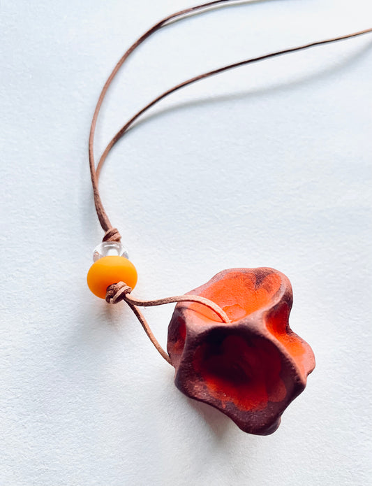 Handcrafted ceramic pendant adorned with glass beads, hanging from a leather cord, combining artisanal craftsmanship with bohemian style.