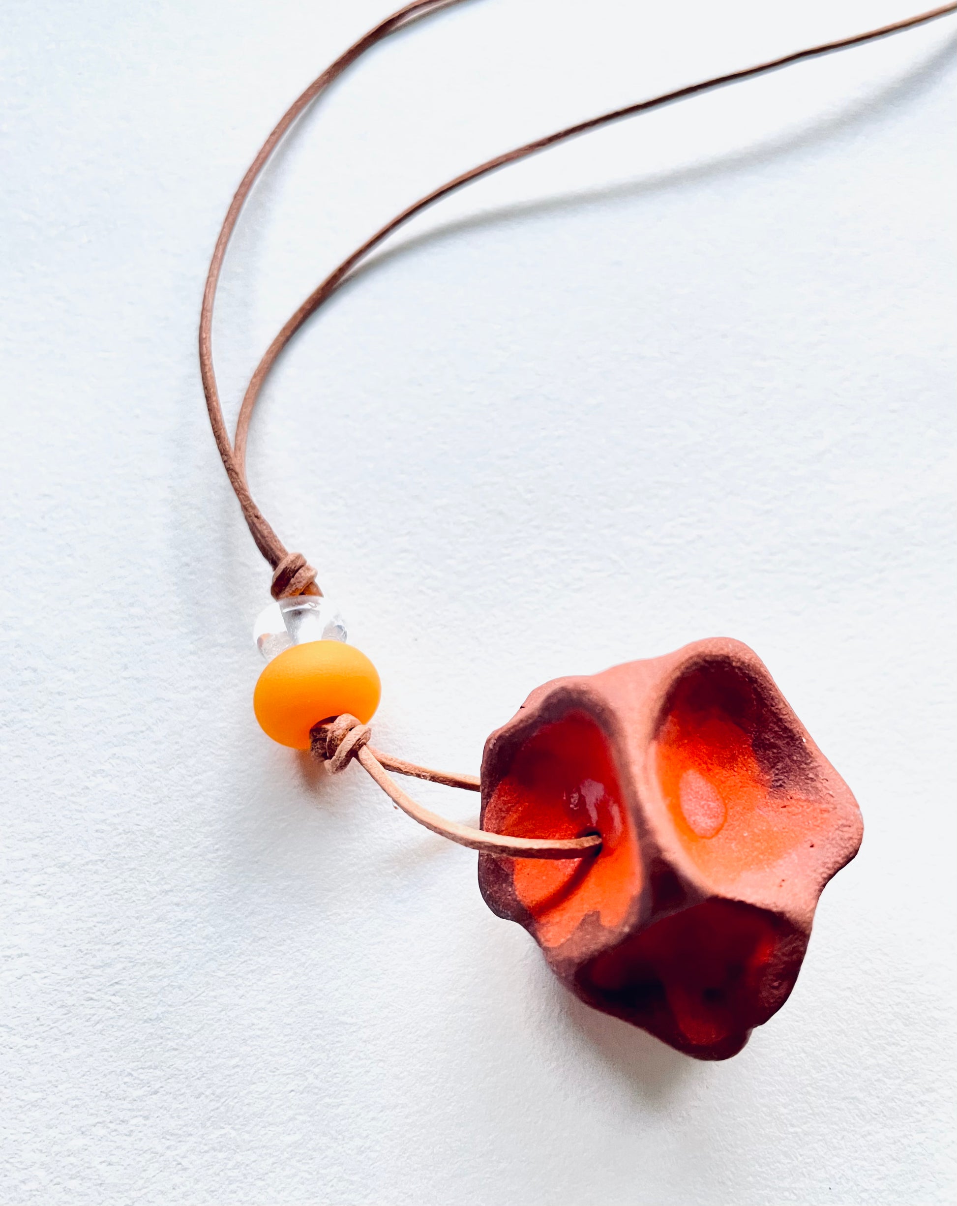 Rustic ceramic pendant with colourful glass beads, strung on a leather cord, highlighting a mix of earthy tones and vibrant details.