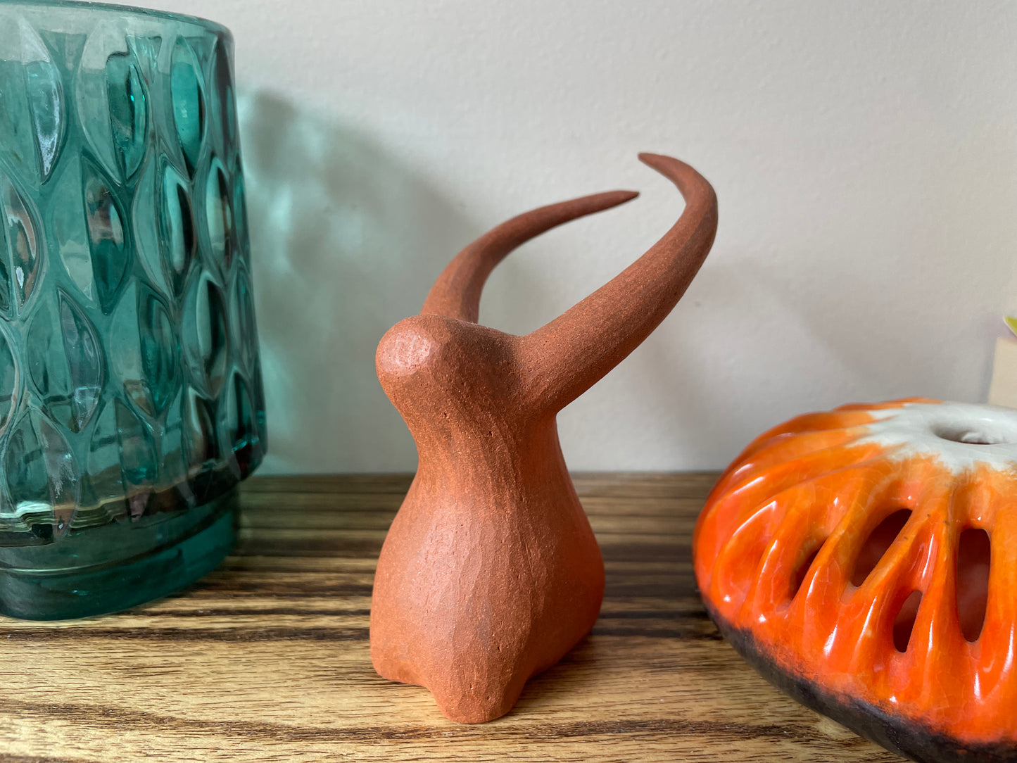 Yak figurine with a minimalistic design, hand-carved and placed on a shelf among other items, blending its natural beauty with the surrounding decor to create a harmonious display.