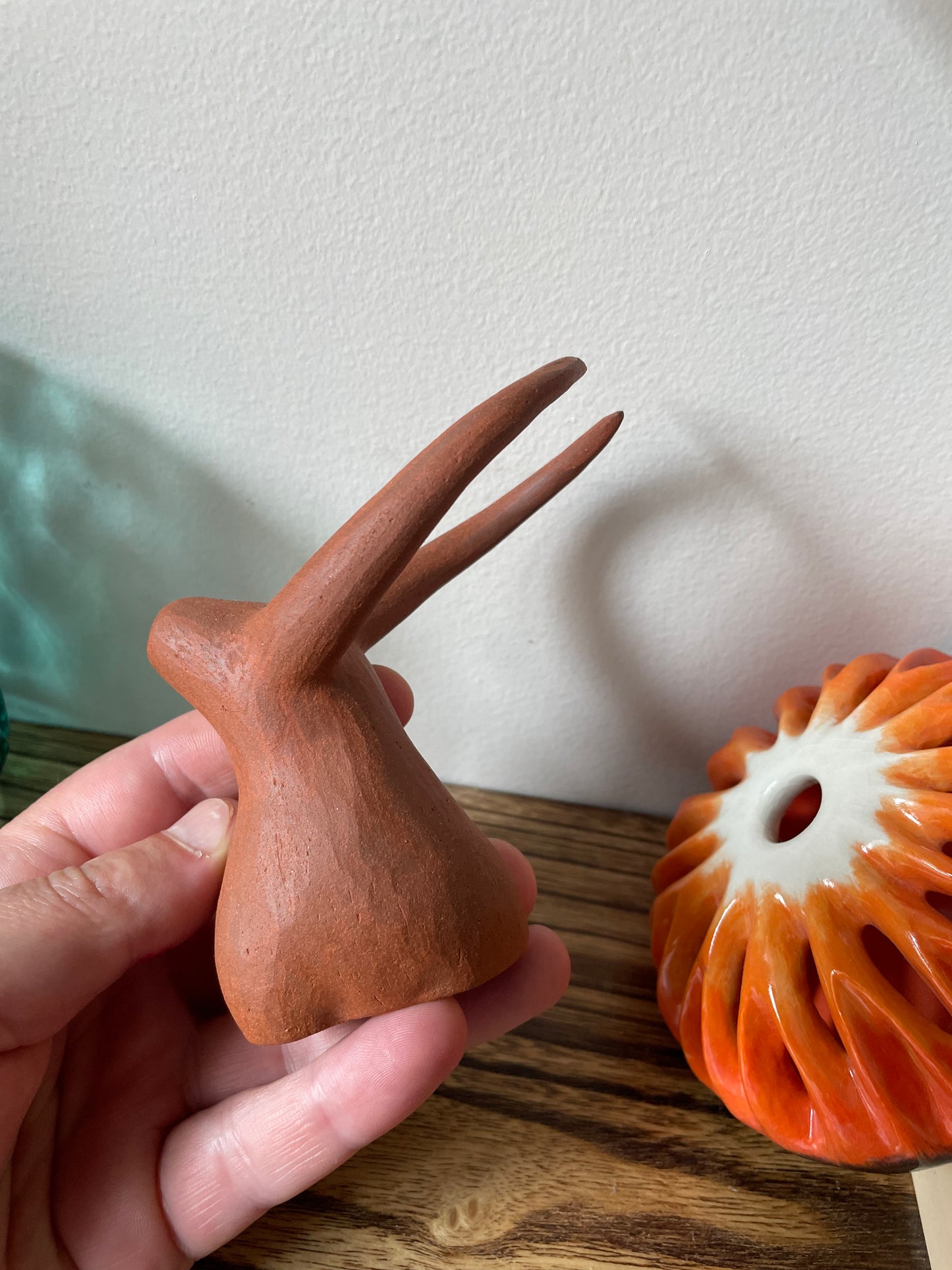 Hand holding a yak figurine, side view, set against a backdrop of a shelf filled with other decorative pieces, showcasing the figurine's unique design and the artisanal craftsmanship from a different perspective.