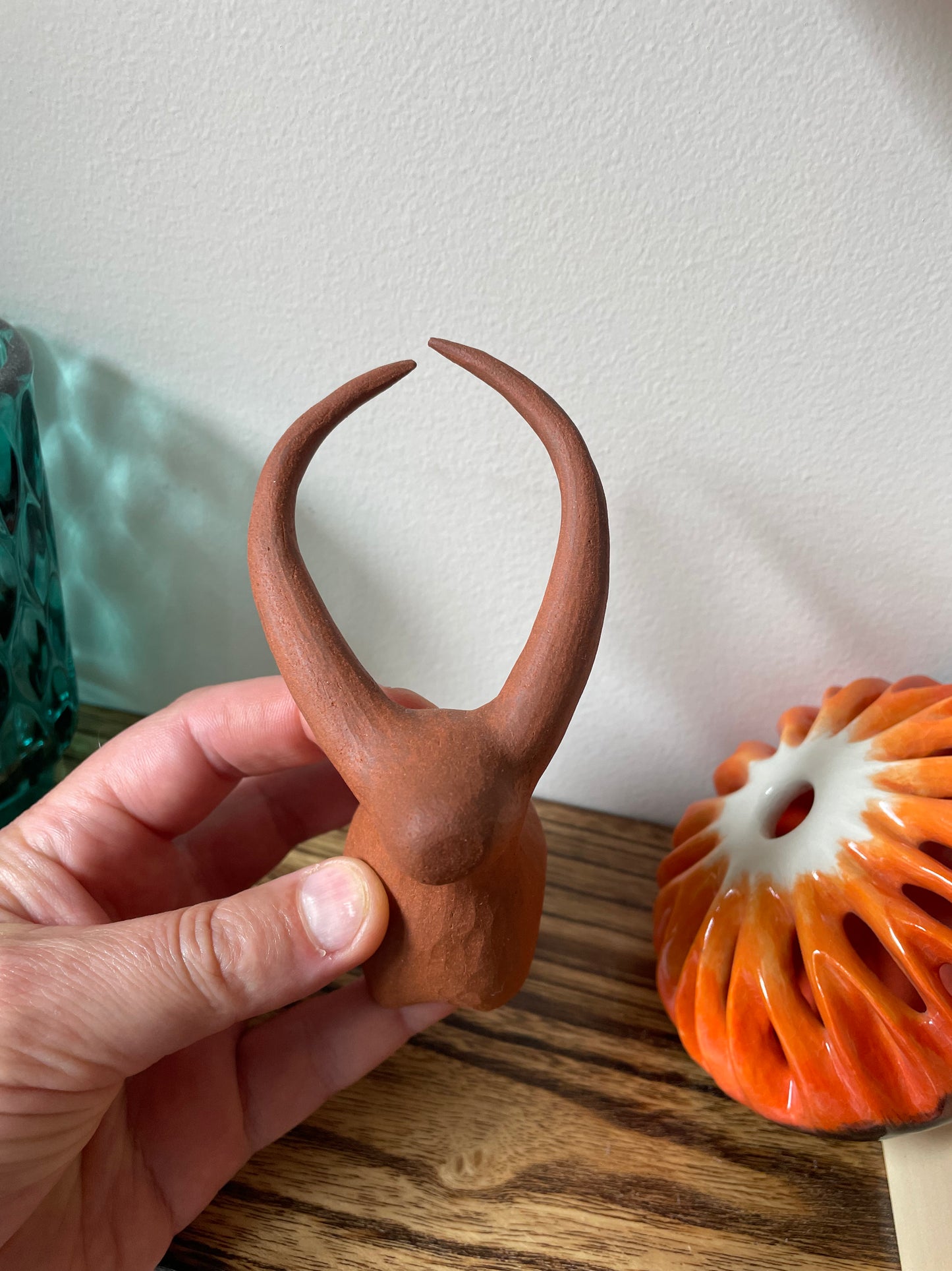 Hand holding a yak figurine, front view, set against a blurred backdrop of a shelf filled with other decorative pieces, highlighting the figurine's natural charm and the beauty of its craftsmanship.