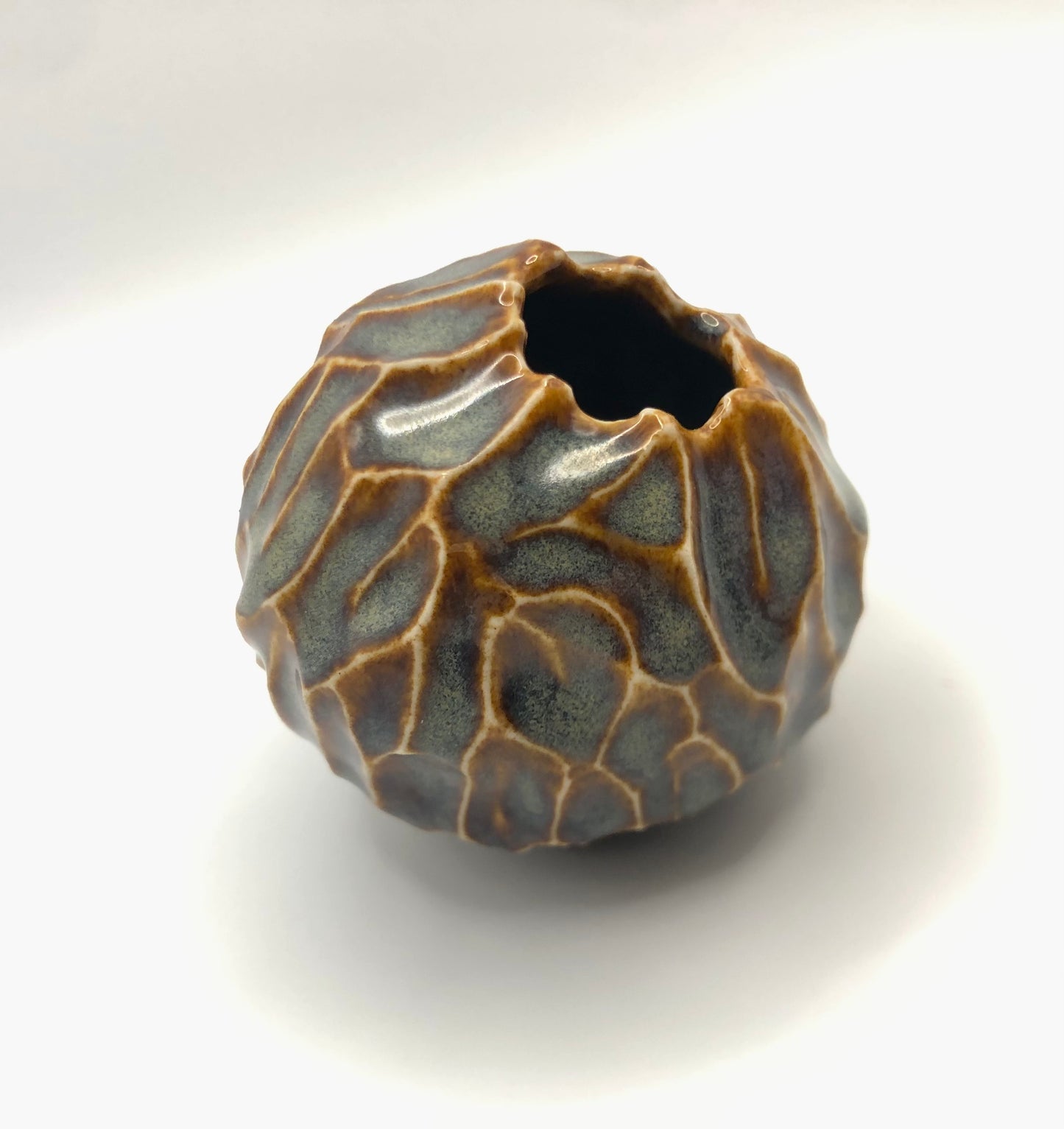 Close-up photograph of a carved vase with an iron lustre glaze, showcasing the glaze's unique ability to produce brown tones where thin and blue-gray floats where thick, adding a sophisticated touch to the vase's carved design.