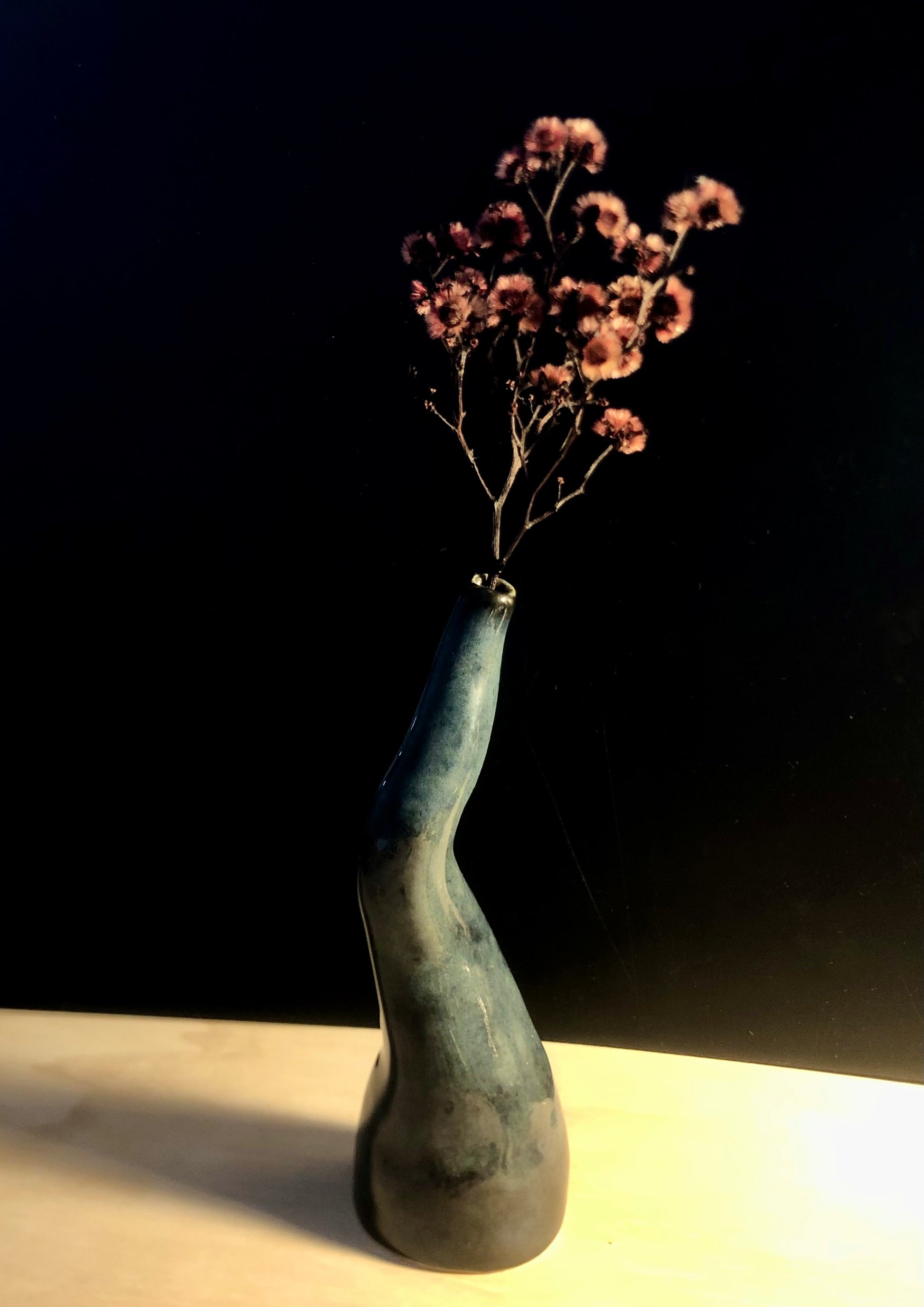 Twisted blue vase featuring a beautiful arrangement of dried pink flowers, creating a unique and visually appealing centrerpiece that combines natural elements with artistic flair.